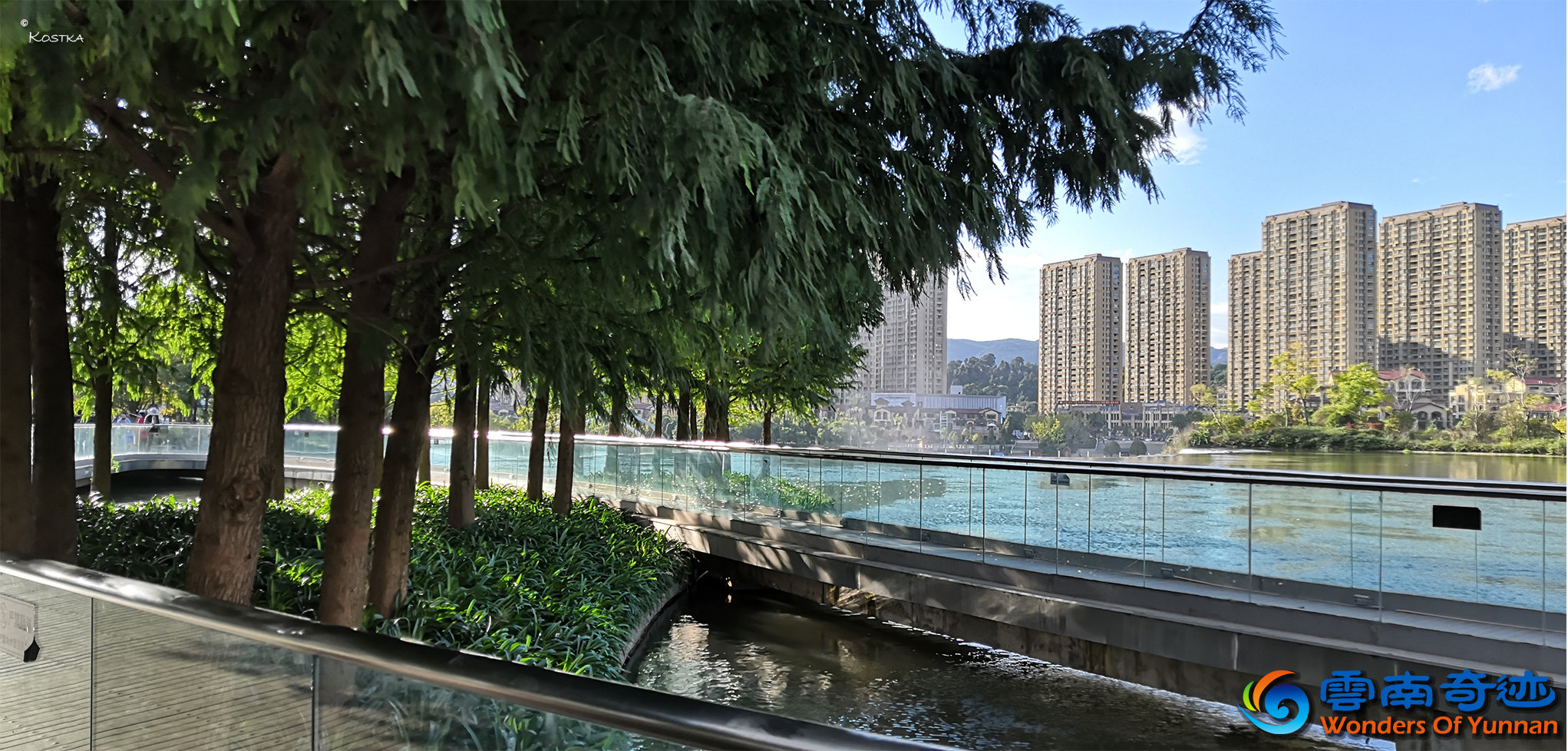 Walking over the glass bridge above the cascades under green trees listening to the waterfall looking at the cloud of water and fog with a nice view over the surrounding city on a beautiful sunny day